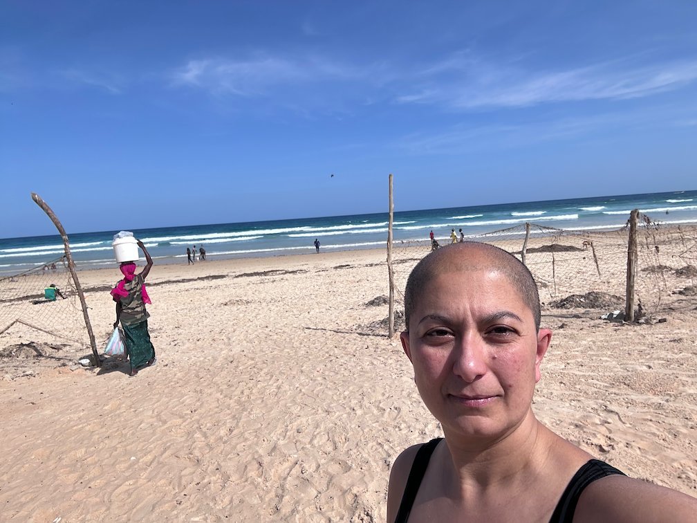 Zayera Khan takes a selfie on Yoff beach with a vendor behind her.