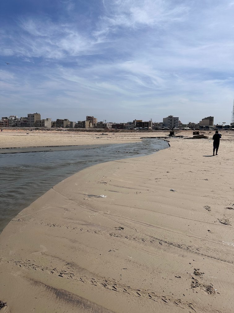 A stream of waste water runs across the sand into the sea at Yoff beach.