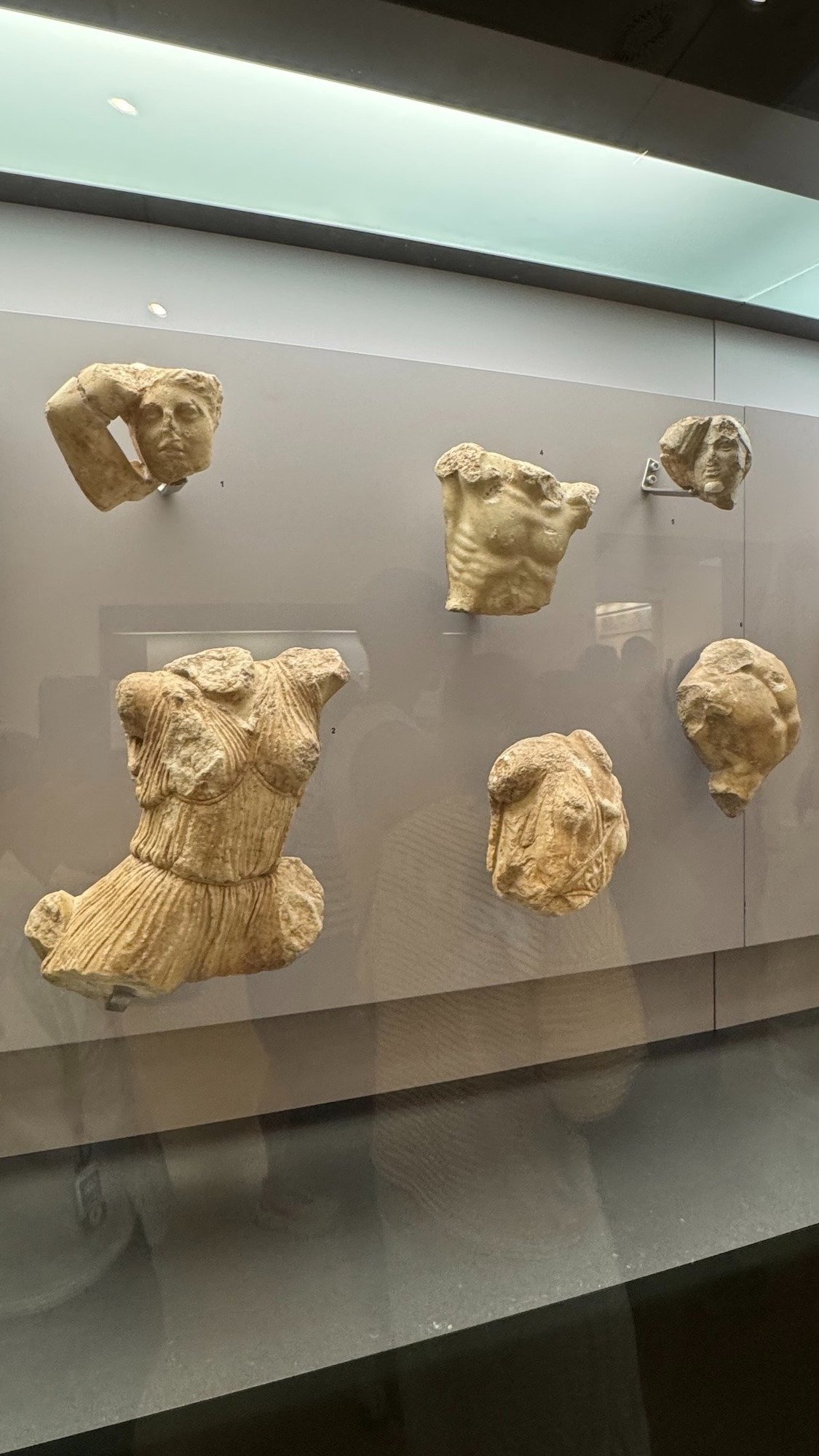 Marble sculpture fragments with heads and bodies behind glass in the Delphi Archaeological Museum