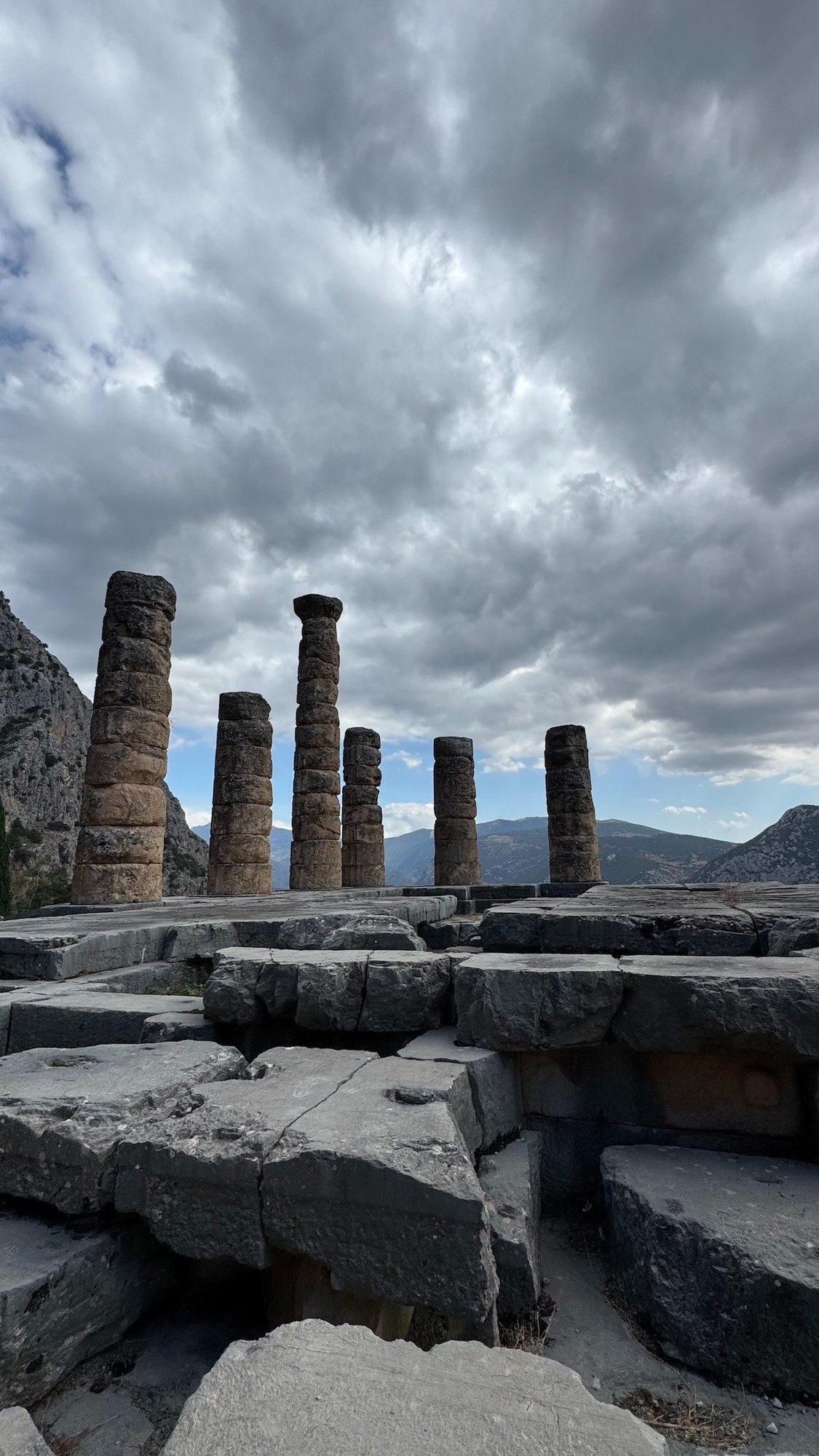 Columns and stone blocks of the Temple of Apollo at Delphi under grey clouds