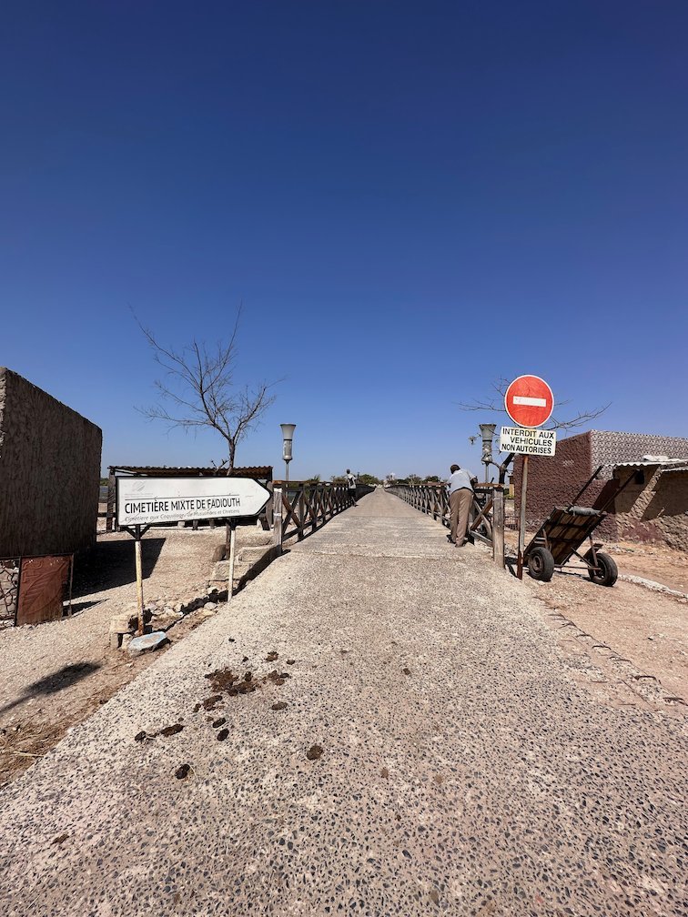 A long bridge with signs leads to the shell island of Fadiouth.