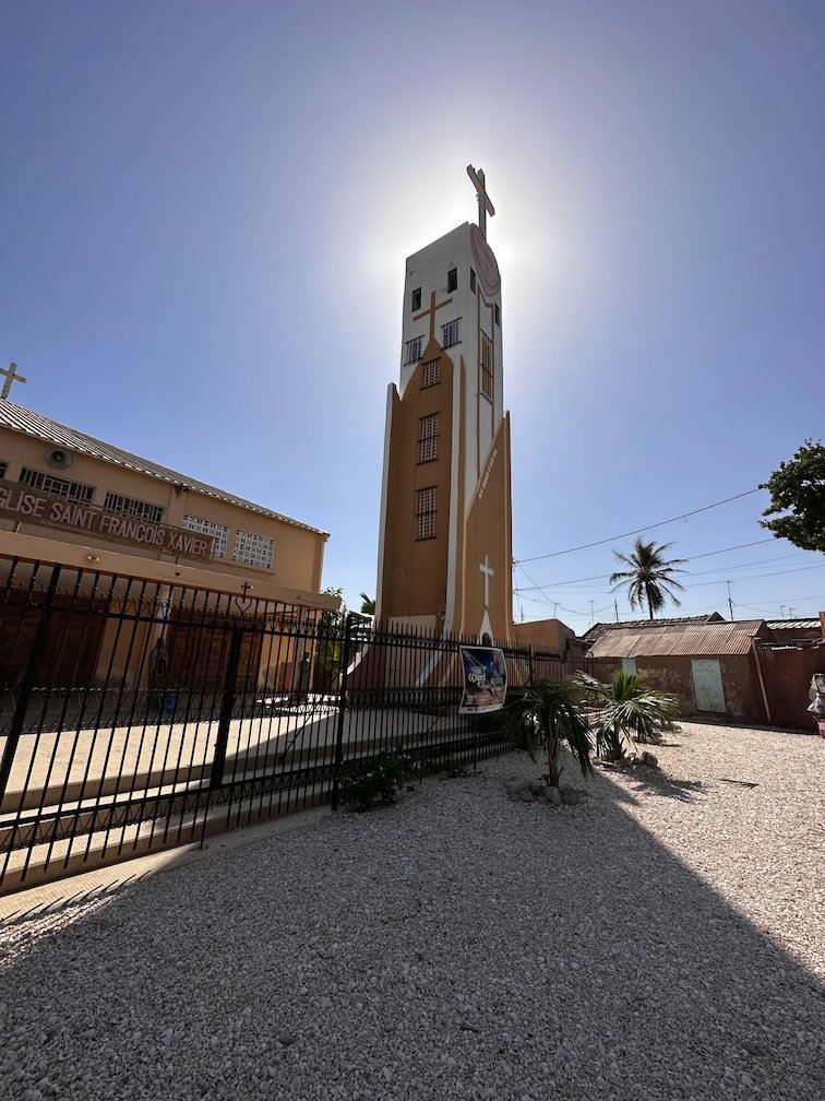 A church tower with a cross stands against the sun in Fadiouth.
