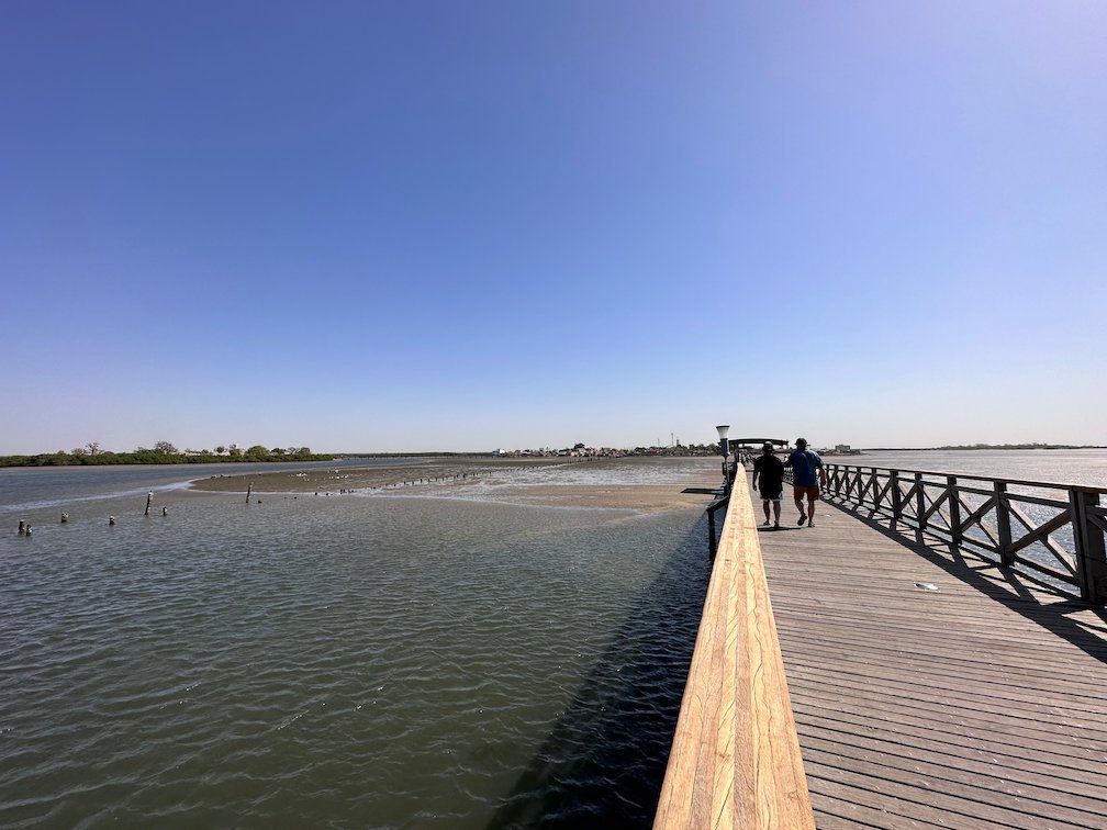 People walk on the wooden bridge over the lagoon to Fadiouth.