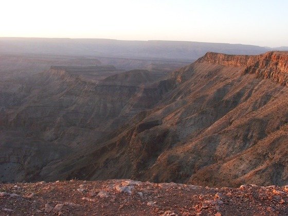 Low evening light colours the steep walls of Fish River Canyon red and brown in Namibia.
