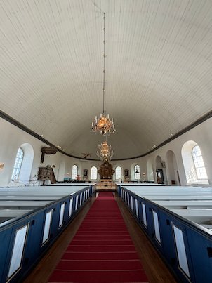 Interior of Fjärås church with a red carpet, blue and white pews, a chandelier and the altar
