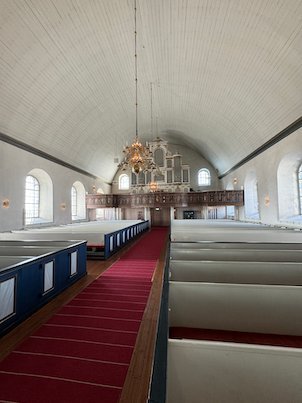 Interior of Fjärås church towards the organ loft, with white pews and a curved wooden ceiling