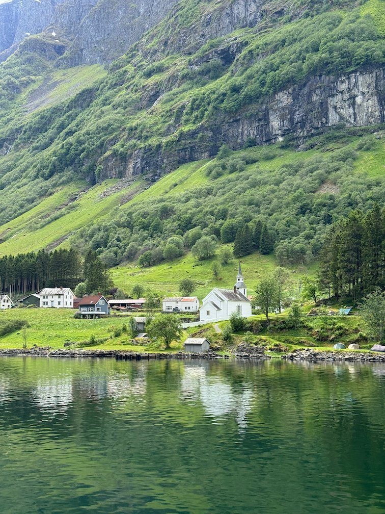 Small fjord village with a white church and green slopes, reflected in the water