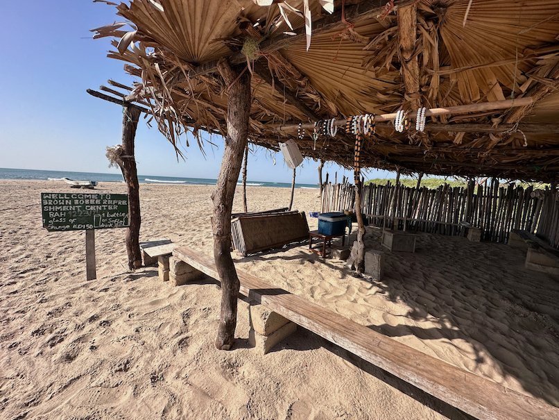 A simple beach bar with a palm leaf roof stands on the sand on the coast of The Gambia.