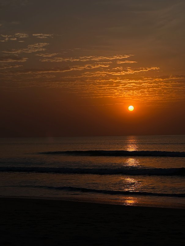The orange sun sets over the Atlantic Ocean from a beach in The Gambia.