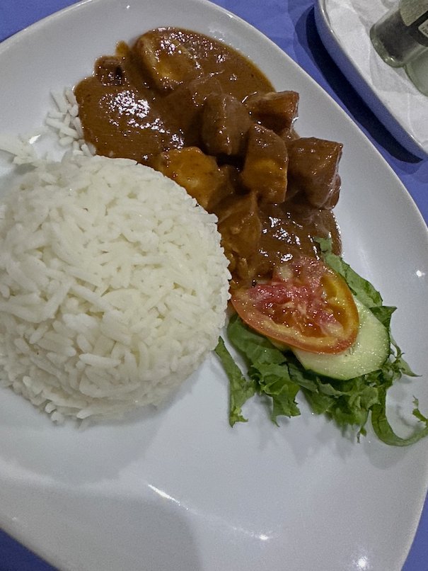 A plate of white rice with meat stew and salad stands on a table in The Gambia.