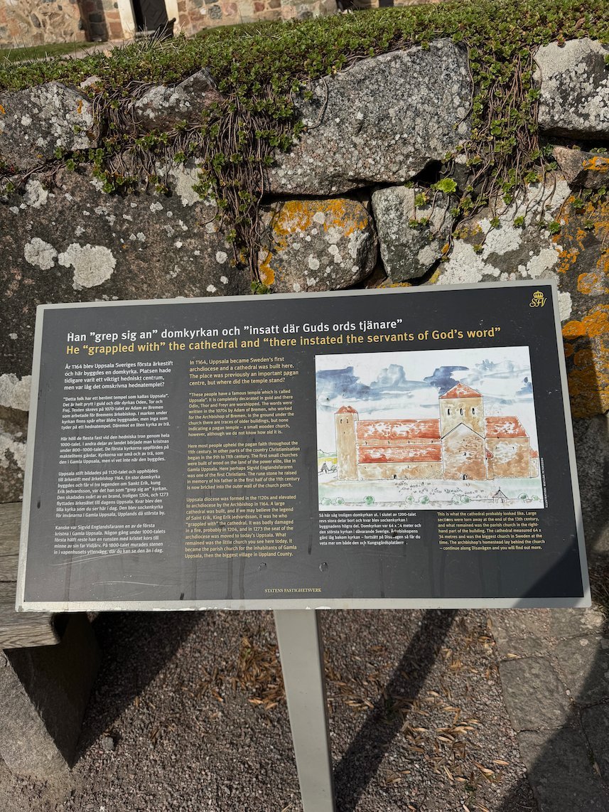 Information sign about the old cathedral at Gamla Uppsala, in front of a dry stone wall