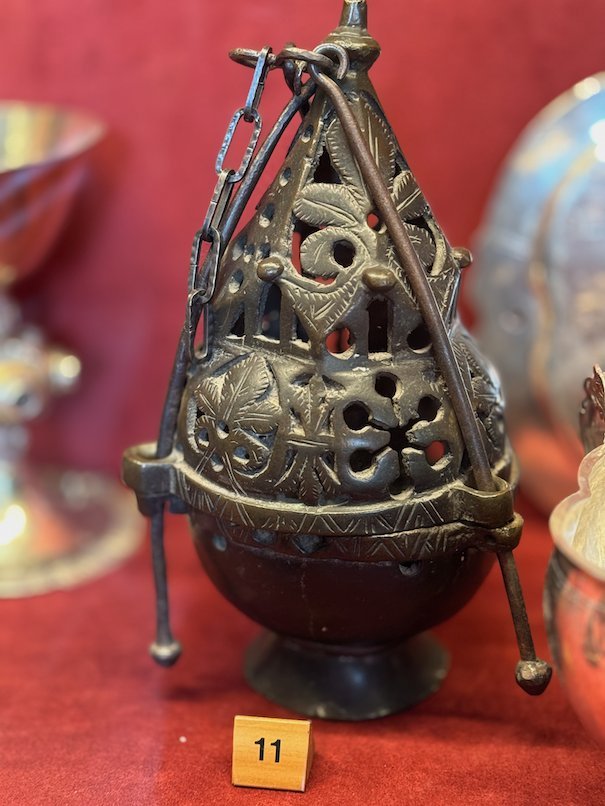 Medieval metal censer with open patterns, on a red cloth in a display case