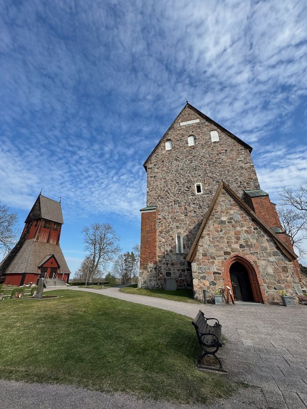 West front of Gamla Uppsala church with its stone tower, and the red wooden bell tower on the left