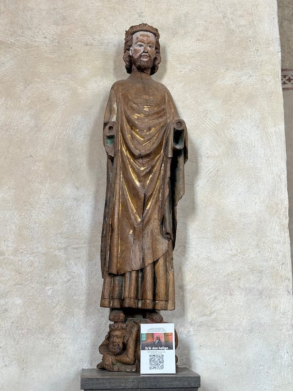 Medieval wooden statue of a crowned king in a long robe, against a white church wall