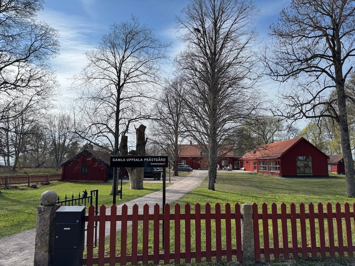 Red wooden buildings and a red picket fence at the entrance to the Gamla Uppsala area, with bare trees