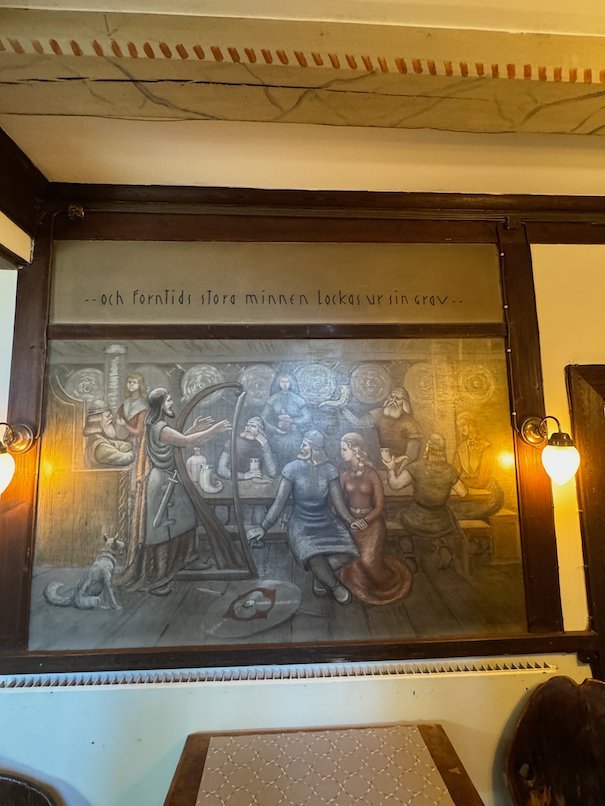 Wall panel at Odinsborg with a relief of people at a feast and a line of old Swedish text above