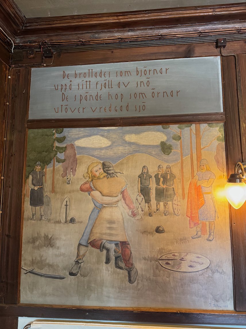 Painted wall panel at Odinsborg with warriors in a Norse scene and old Swedish verse above
