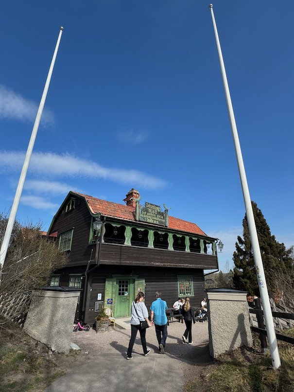 Odinsborg, a dark wooden house with a red roof and two tall flagpoles, with visitors walking in front
