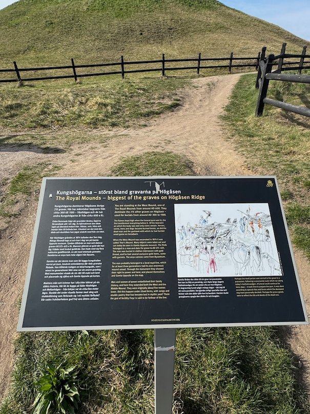 Information sign about the Royal Mounds on the Högåsen ridge, with a path and a grass mound behind
