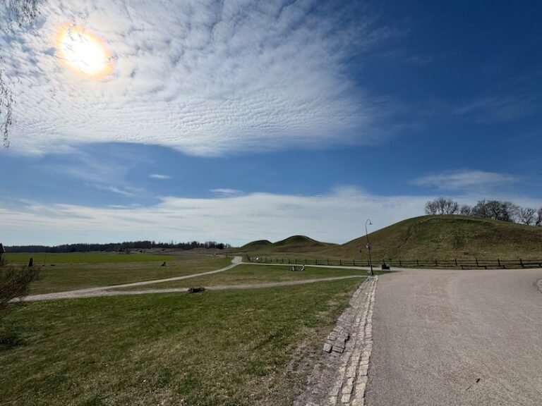 Wide view of the royal mounds at Gamla Uppsala, with a path, green grass and a blue sky
