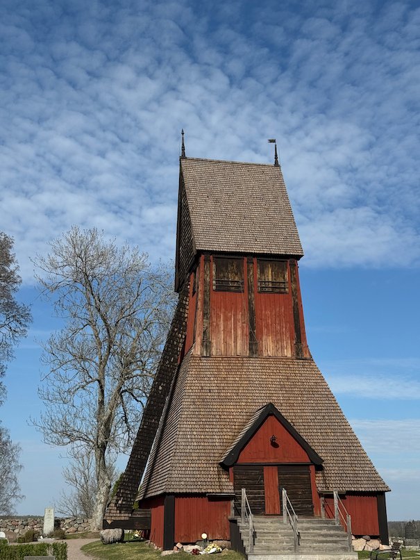 Tall red wooden bell tower with a shingle roof at Gamla Uppsala church