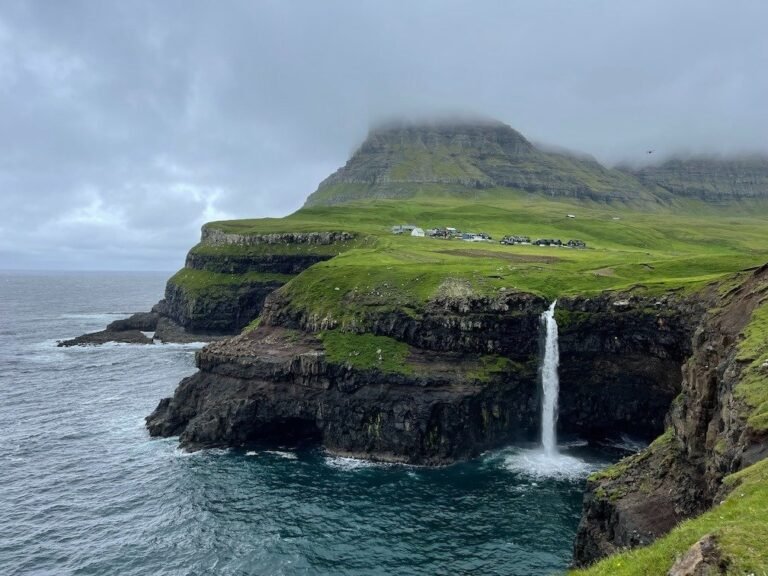 The Mulafossur waterfall drops into the sea below the village and a green mountain.