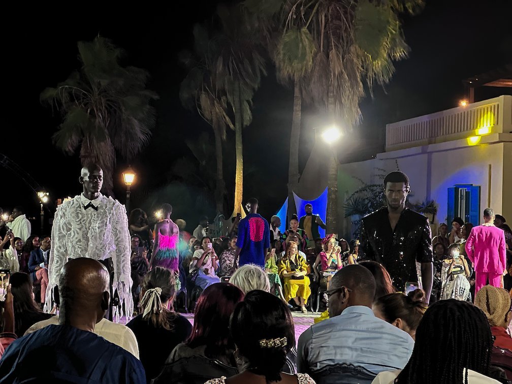 Models in bold clothes walk in front of the audience on Goree Island.