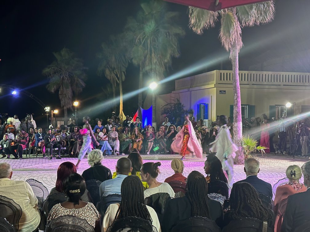 Models walk on a lit stage at a night fashion show on Goree Island.