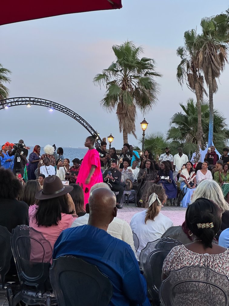 A model in a pink dress walks past the audience on Goree Island.