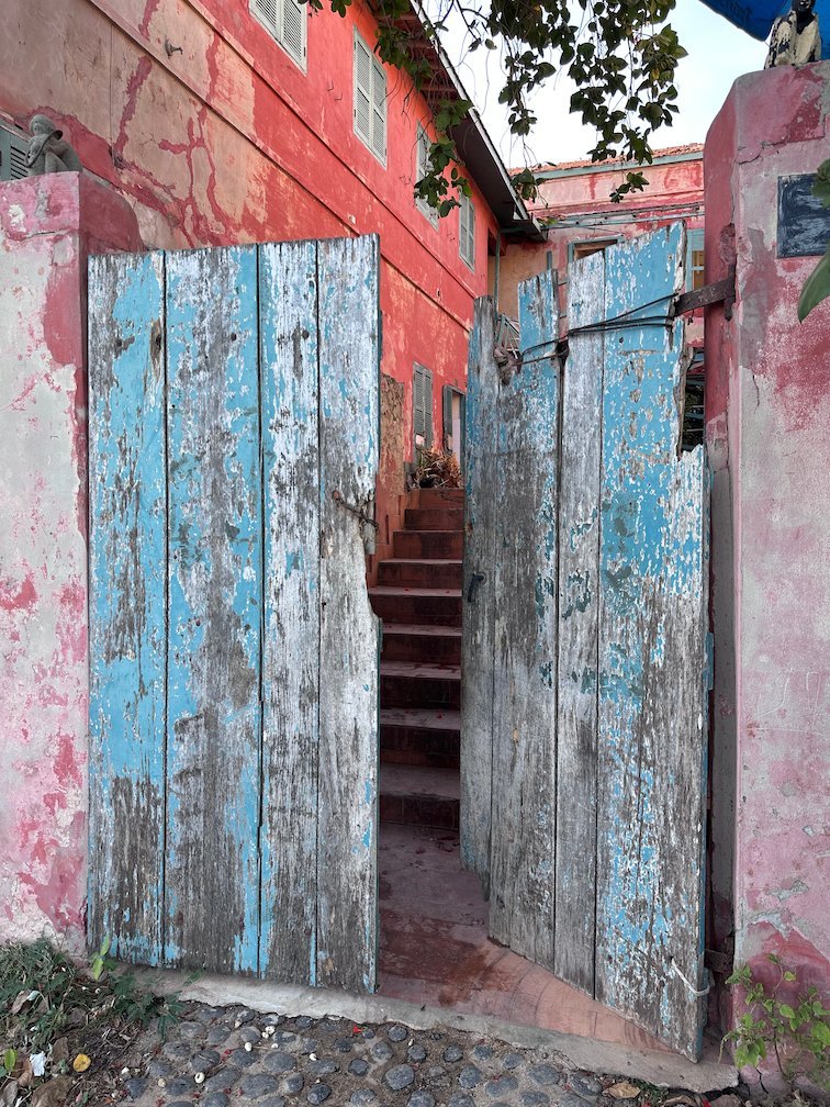 Old blue wooden doors open to a narrow stair on Goree Island.