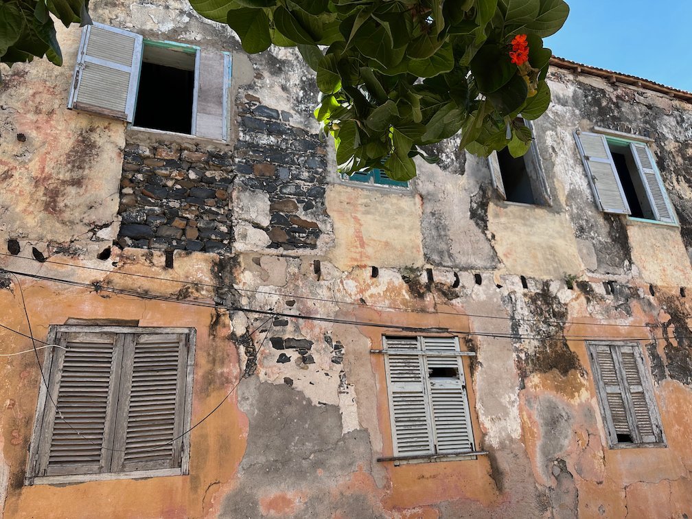 An old orange facade with wooden shutters is falling apart on Goree Island.