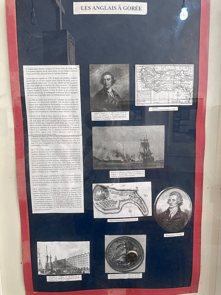 A museum board shows texts and pictures about the English on Goree Island.