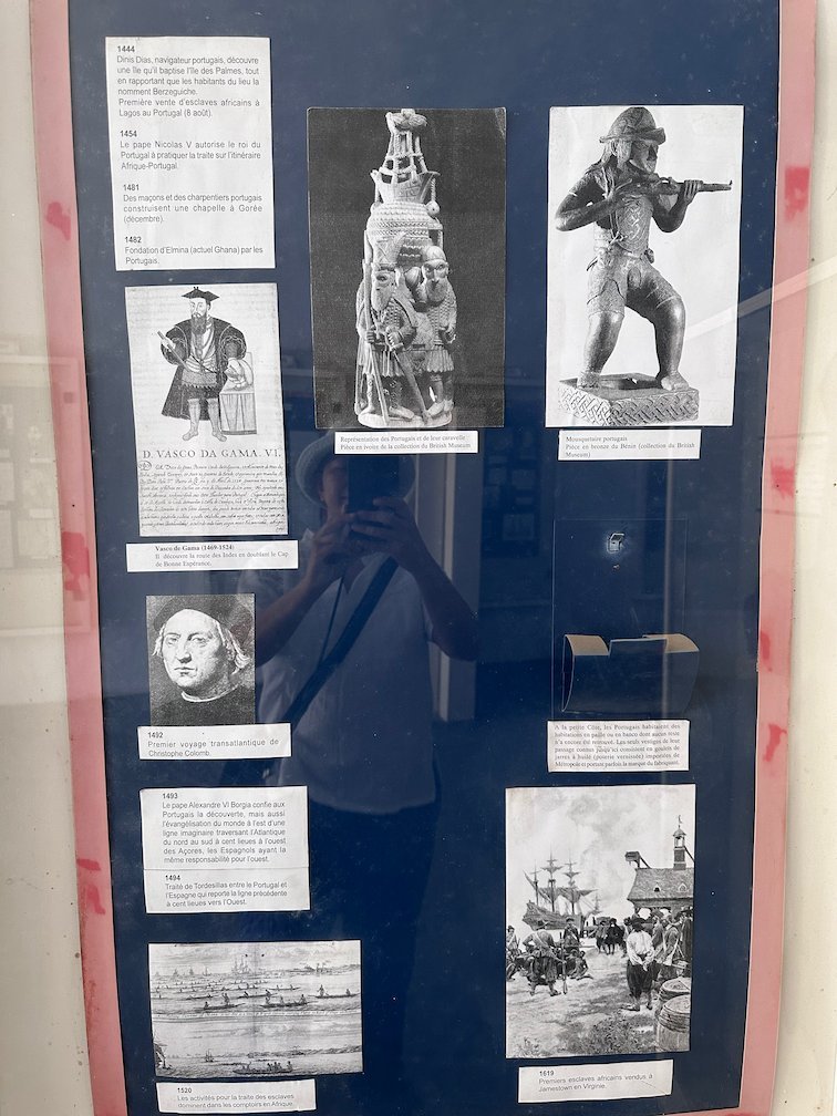 A museum board shows old pictures of statues and ships on Goree Island.