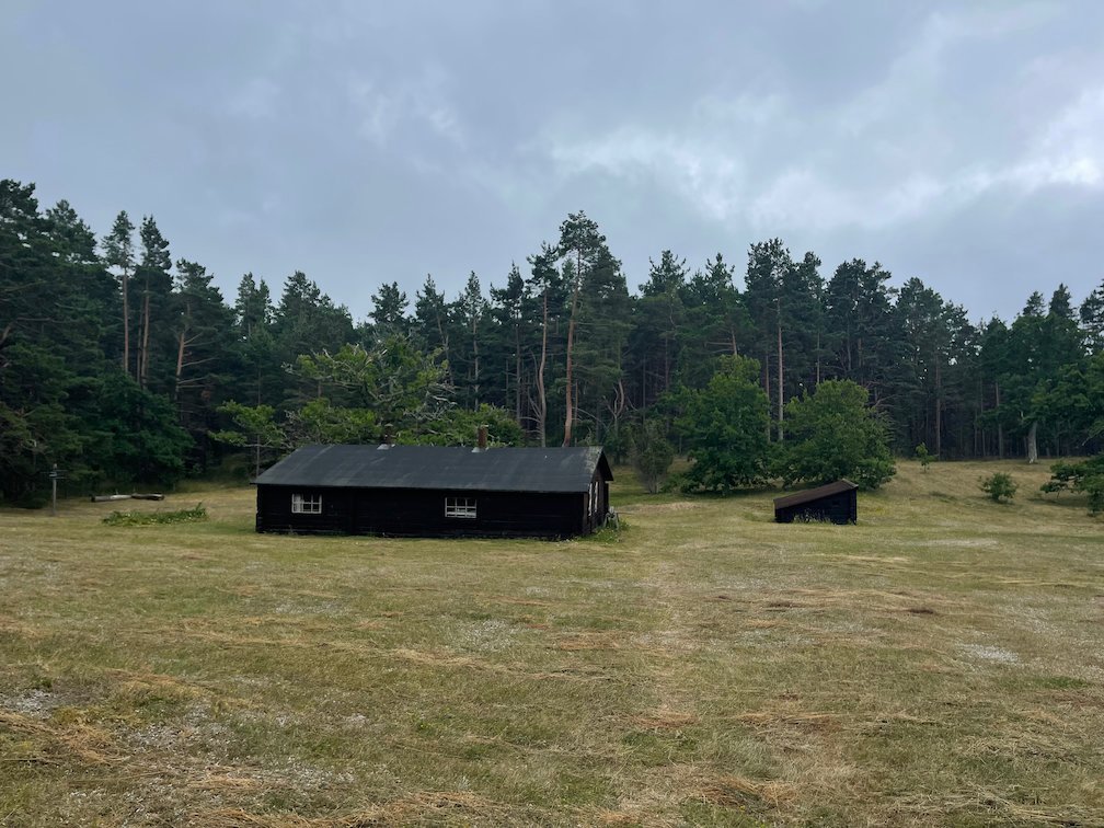 Svarta trähus på en öppen äng vid skogskanten, Gamla gården