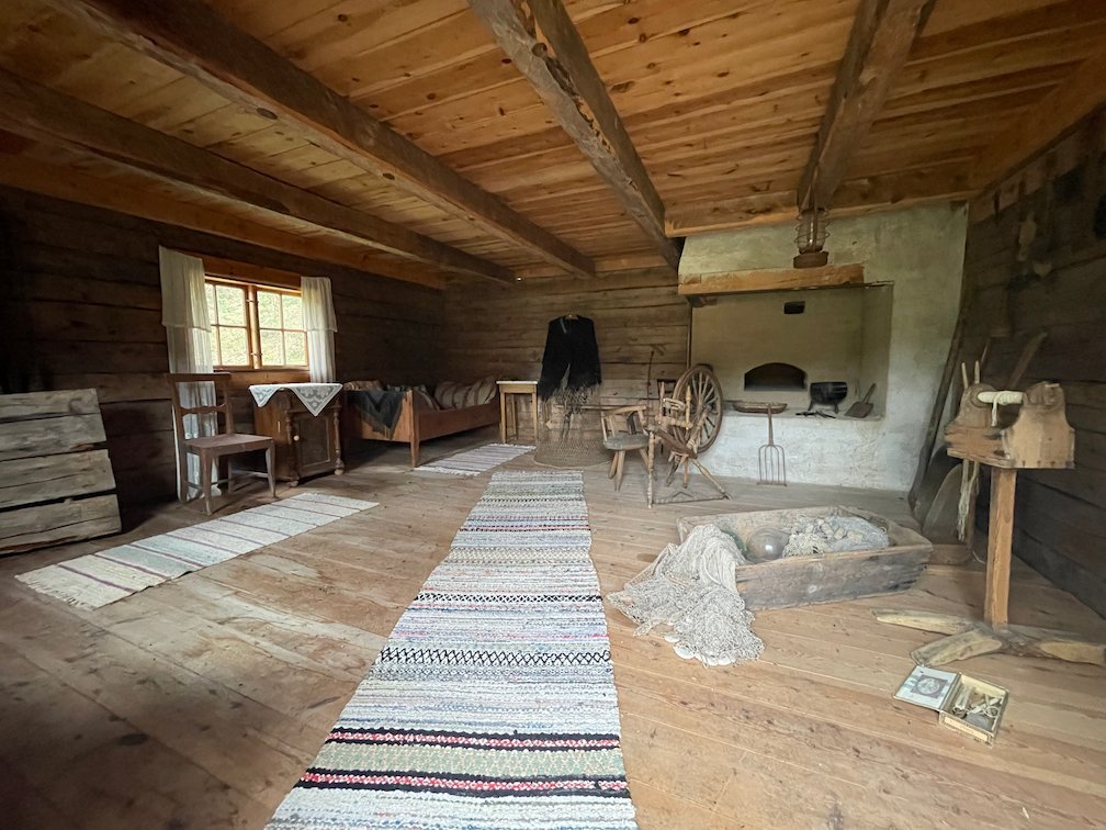 Insidan av den gamla stugan på Gamla gården, Gotska Sandön, med trasmatta, spinnrock och öppen spis