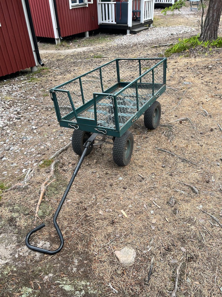 Grön dragvagn för bagage framför röda stugor på lägerplatsen
