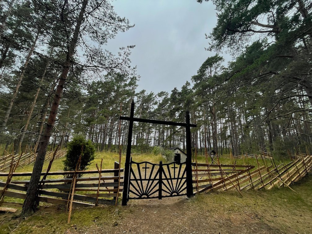 Svart järngrind och gärdesgård vid kyrkogården i tallskogen