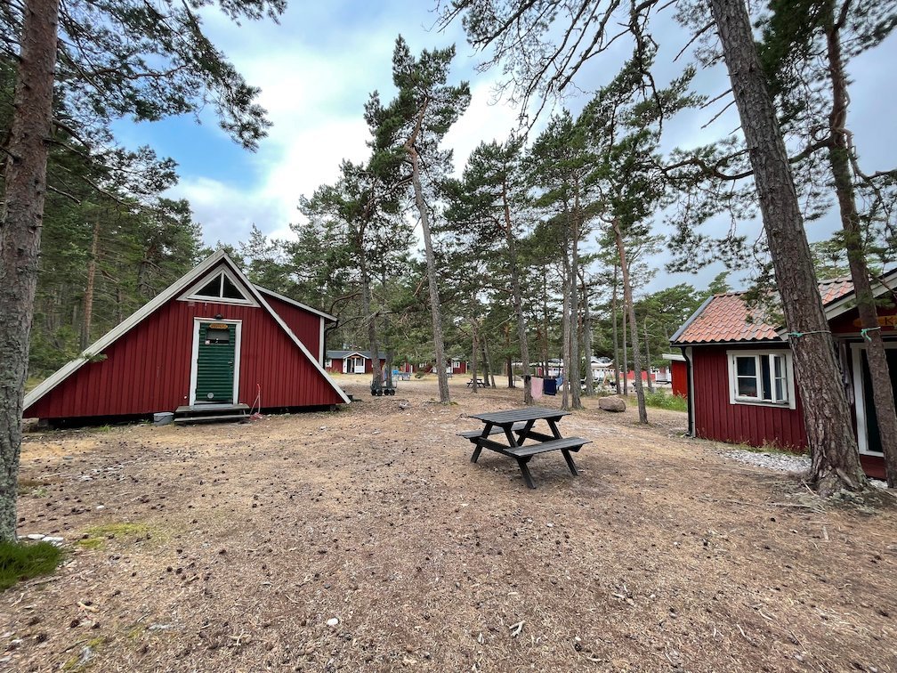 Röda stugor och ett picknickbord bland tallar på lägerplatsen