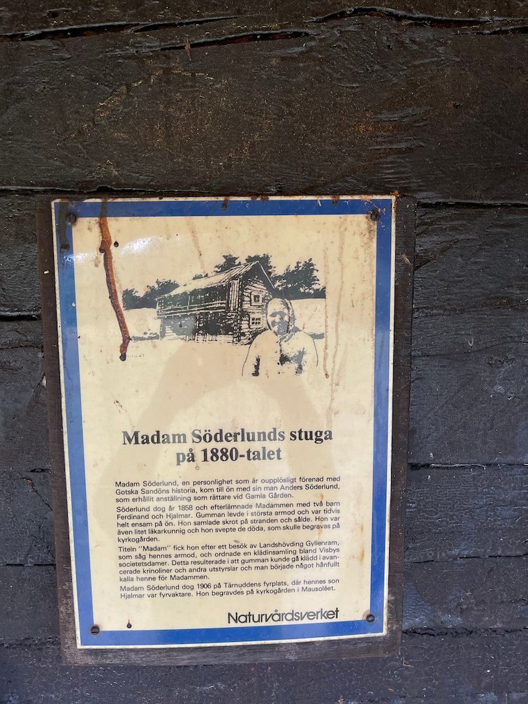 Skylt Madam Söderlunds stuga på 1880-talet på en svart trävägg