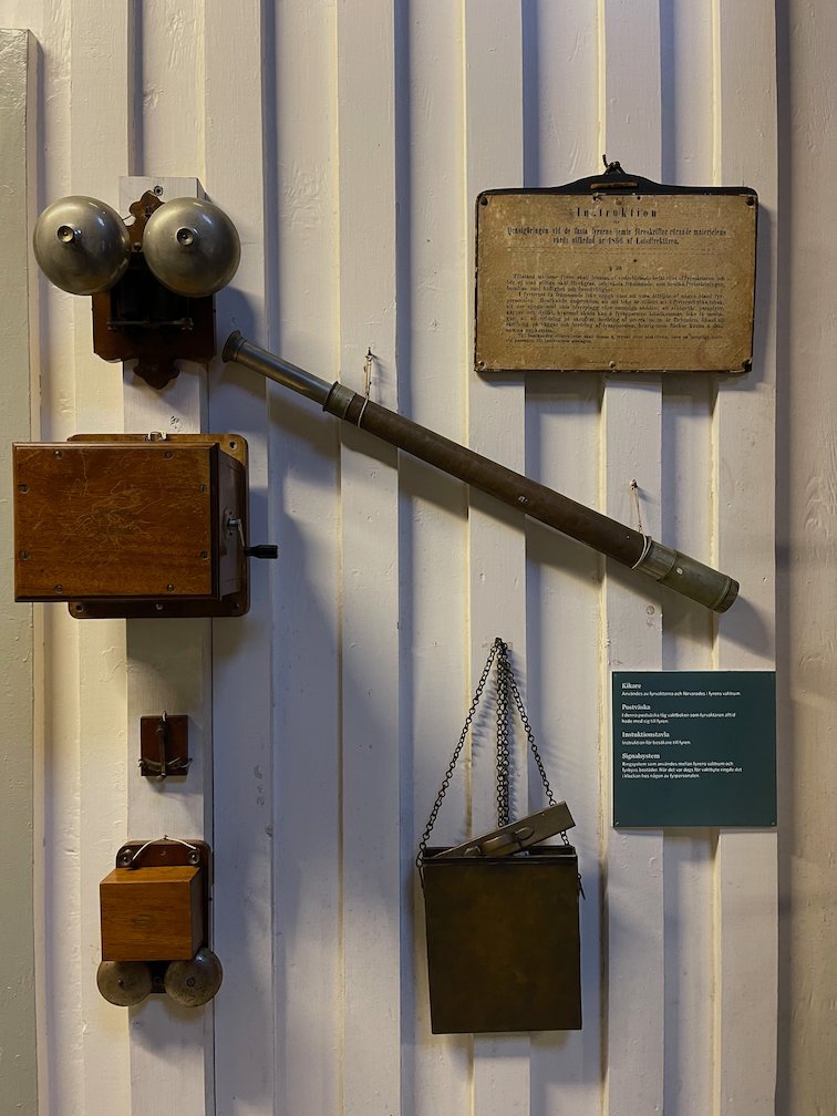 Gammal väggtelefon och andra föremål på en vit vägg i museet