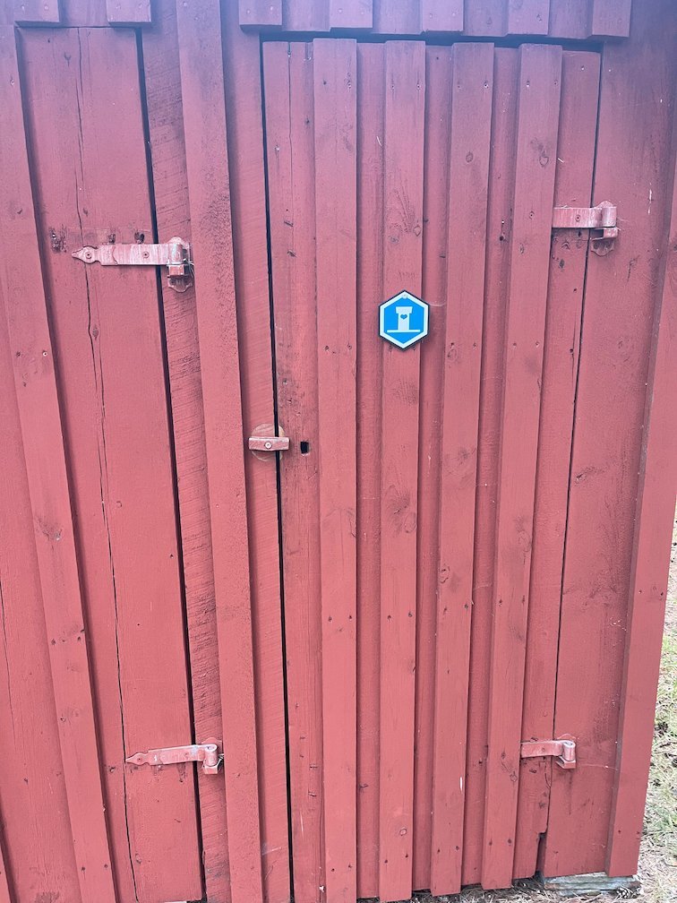 Röd trädörr med blå skylt till en torrtoalett på Gotska Sandön