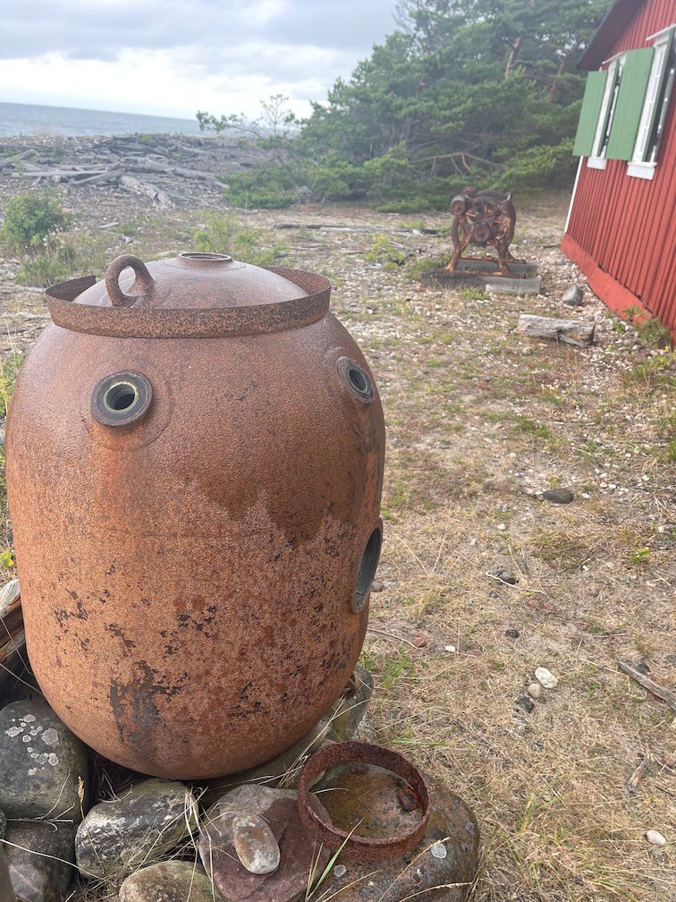 Rostig järntunna framför en röd stuga vid havet på Gotska Sandön