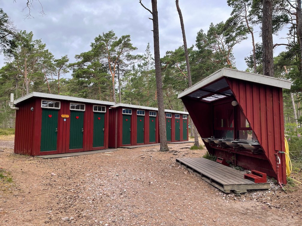 Röda torrtoaletter och en utomhusdisk på lägerplatsen