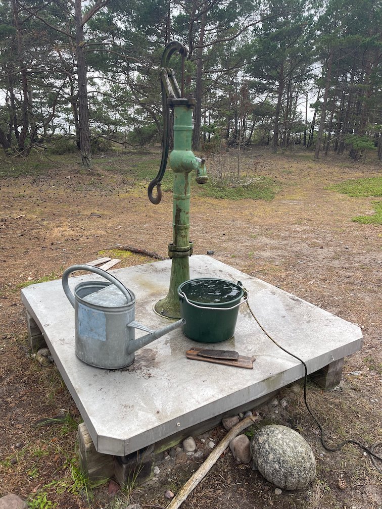 Grön vattenpump med vattenkanna och hink vid tältplatsen Nymans, Gotska Sandön