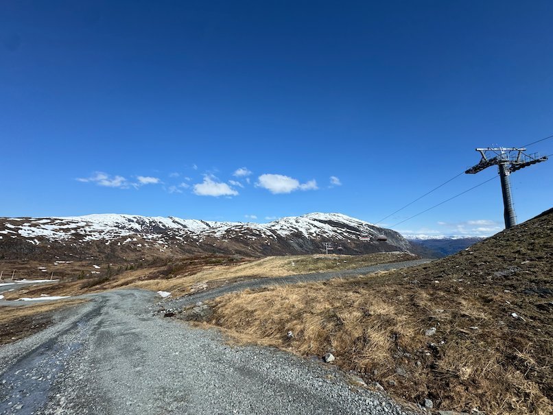 Gravel road and a ski lift pylon on Hanguren, with snowy mountains under a blue sky