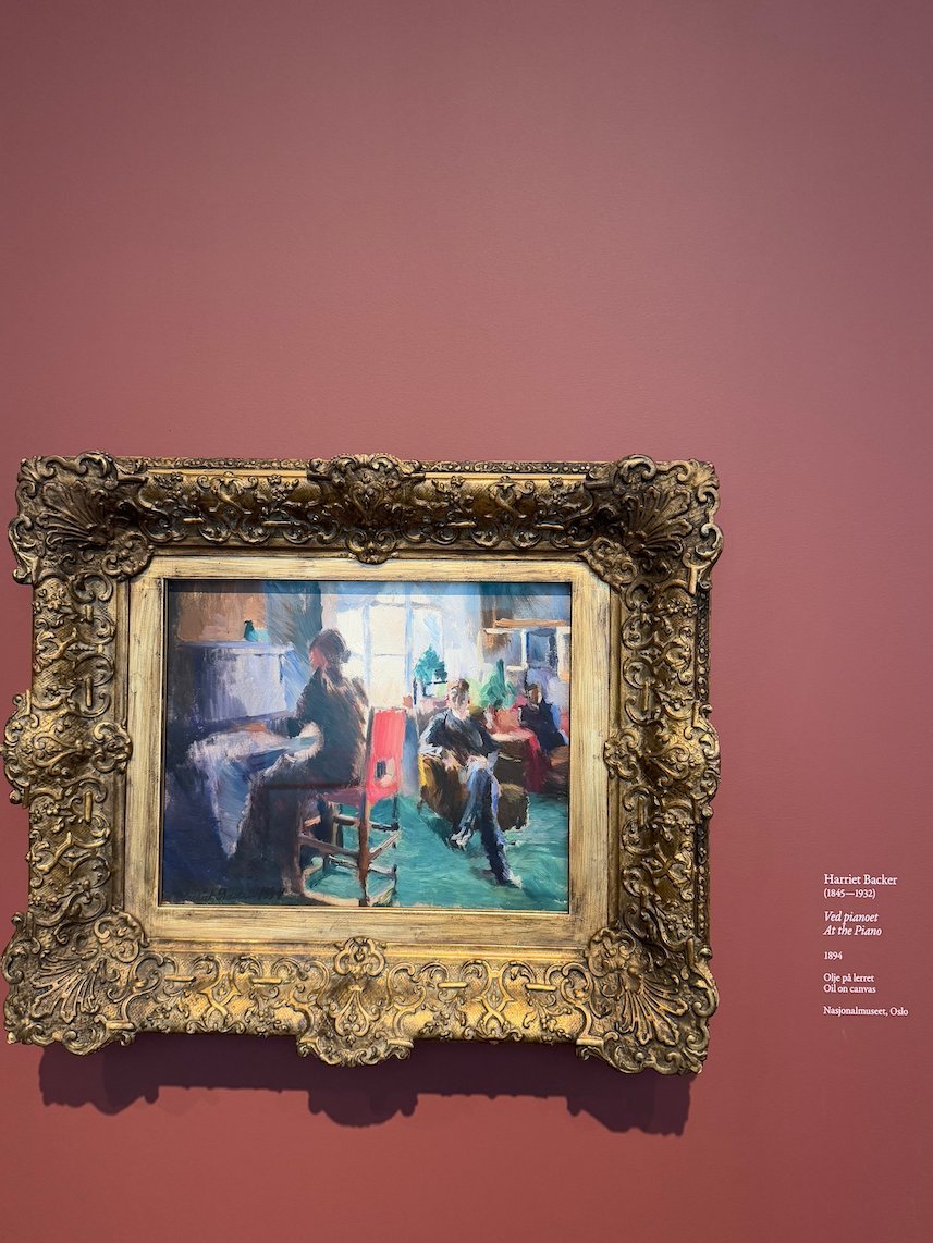 Painting by Harriet Backer of women in a bright room, on a red museum wall