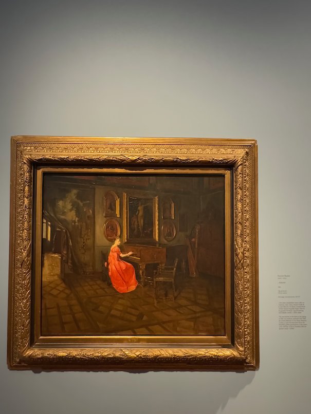 Painting by Harriet Backer of a woman in a red dress at a piano in a dark room