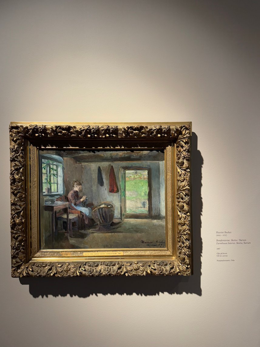Painting by Harriet Backer of a woman at a table by a window, with an open door to a green garden