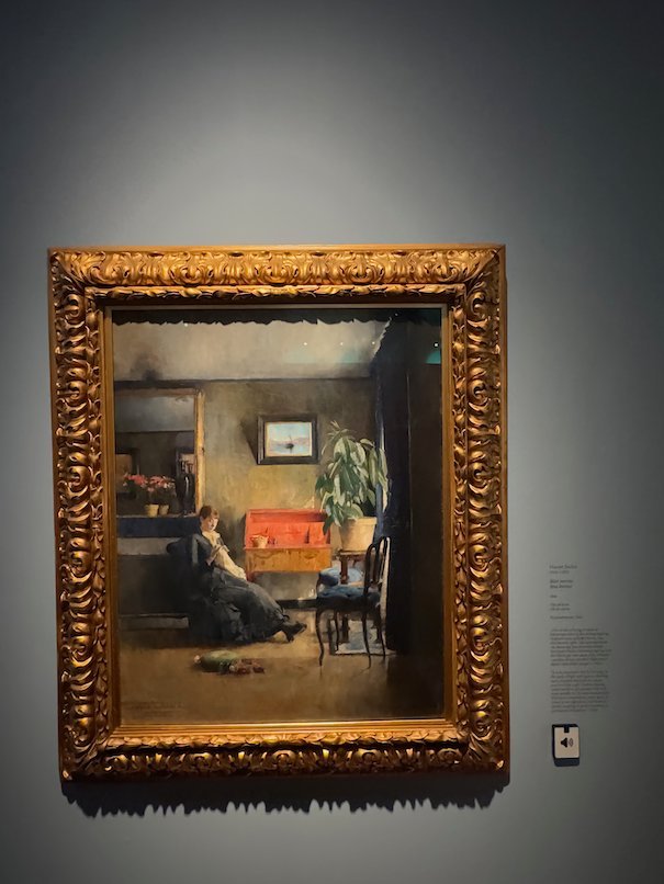 Painting by Harriet Backer of a woman who rests in a room with a red table and plants