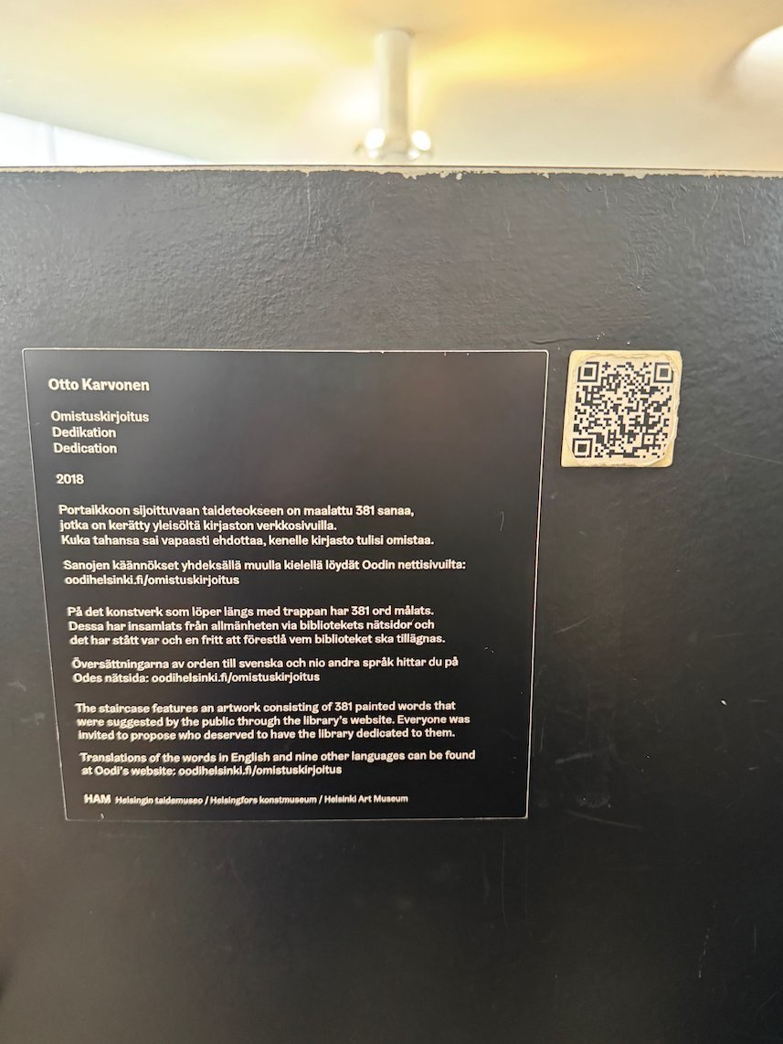 An information plaque with a QR code explains an artwork on a black wall in Oodi library in Helsinki.